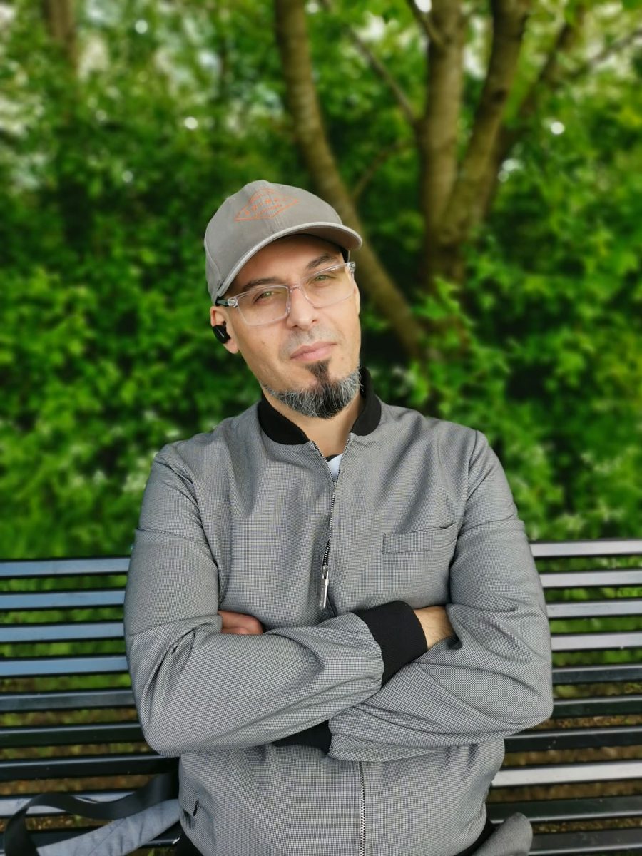 Juan, the founder of Alongside AI, outdoors in a grey jacket and cap, with his arms folded